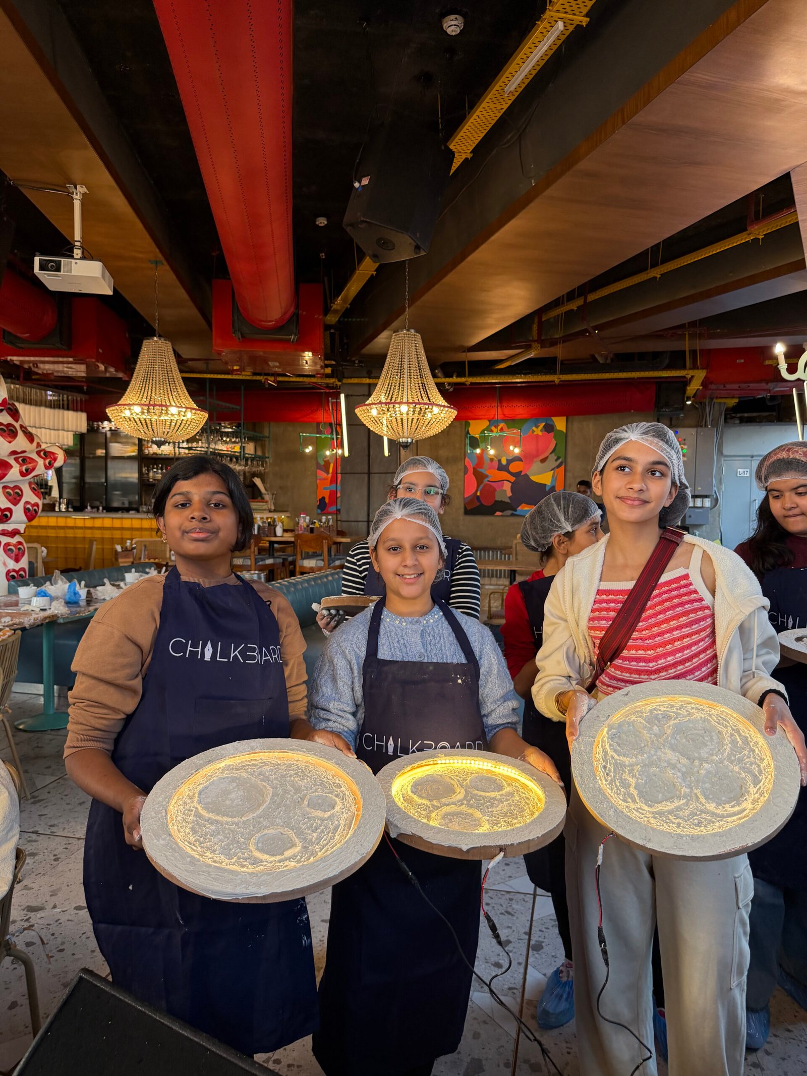 Participants displaying their glowing moon art creations during a Chalkbooard workshop session.